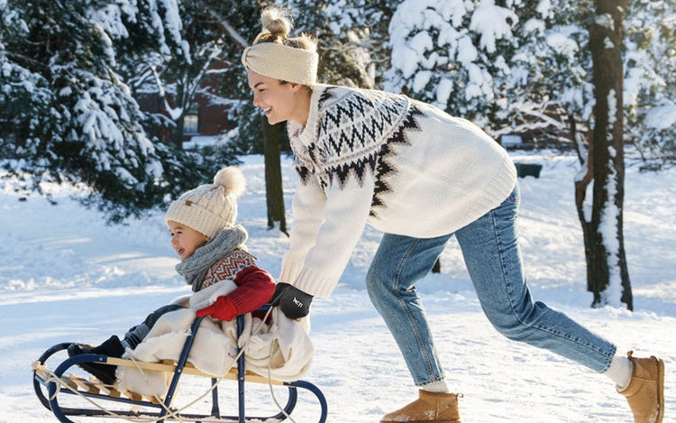 A woman wearing cold weather gloves is playing sled with a child.