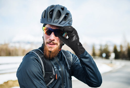 Cyclist wearing MCTI cycling gloves on snowy mountain road in winter, adjusting glasses for optimal vision and warmth.